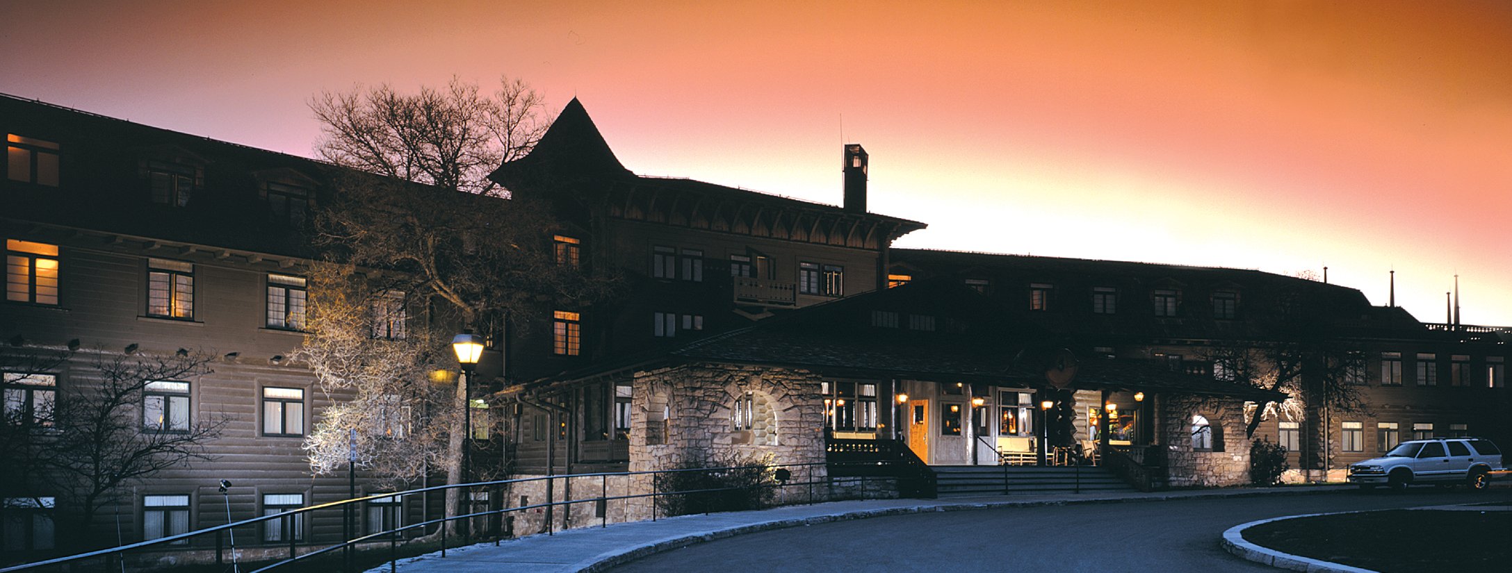 The sun sets behind the El Tovar Hotel, creating a stunning orange sky.