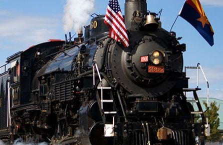 A black steam engine train with an American flag on the front.